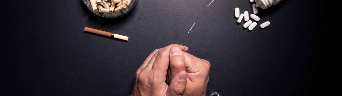 Chained hands on a black table next to cigarettes and pills