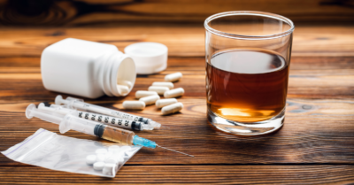 A glass of alcohol with pills and a syringe next to it.