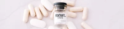 Fentanyl pills and a syringe surrounding a fentanyl bottle