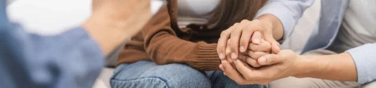 A couple sitting on a couch holds hands and talks to a counselor