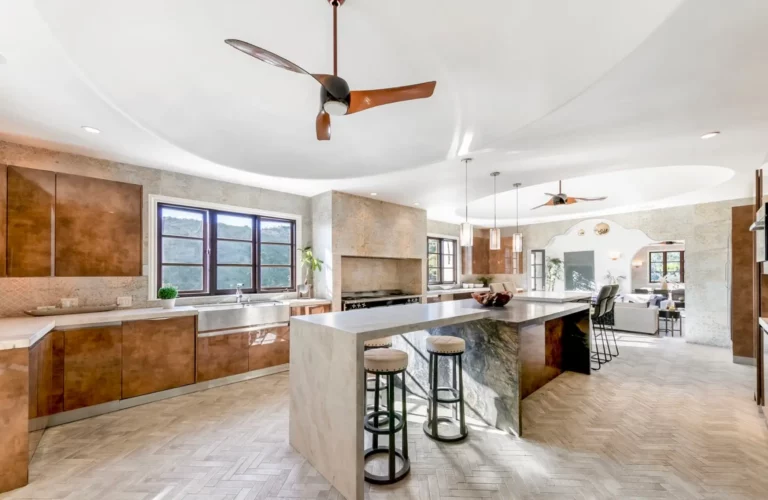 Modern kitchen at Legacy's Los Angeles rehab with light stone floors and counters, wood cabinet accents, and views of the Hollywood Hills