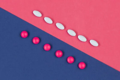 White pills lined up against pink pills across a blue and pink paper.