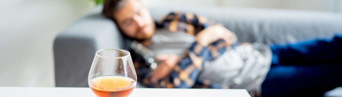 A man sleeping on a couch with a drink in the foreground.