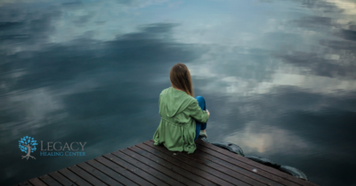 A woman sits on a dock next to a lake - stares off into the distance.